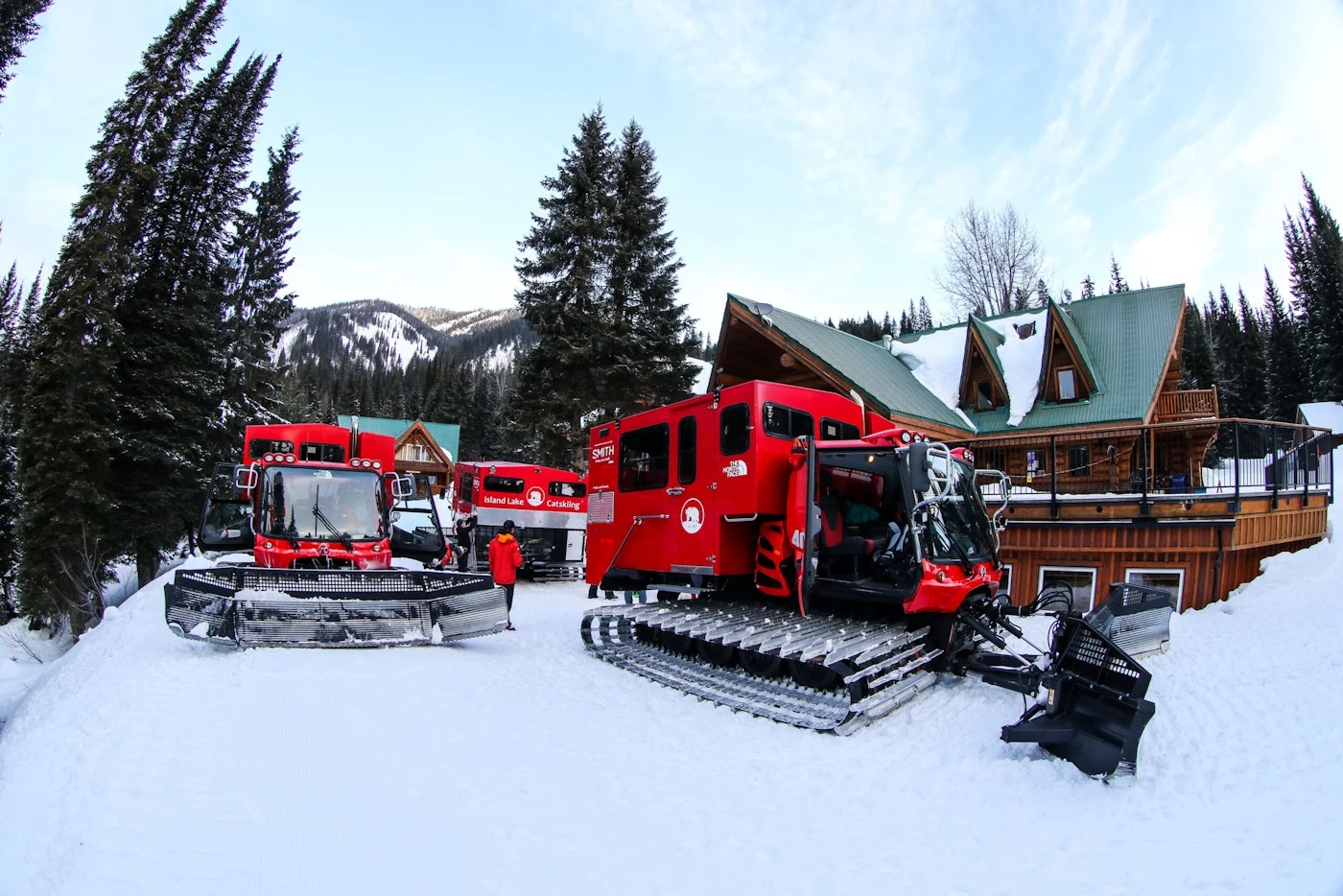 Red snowcats gathered outside a snow-covered Island Lake lodge