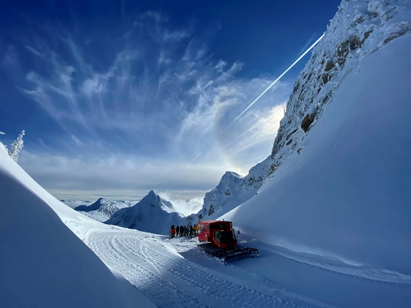 A red Island Lake snowcat on a road between deep alpine snowbanks