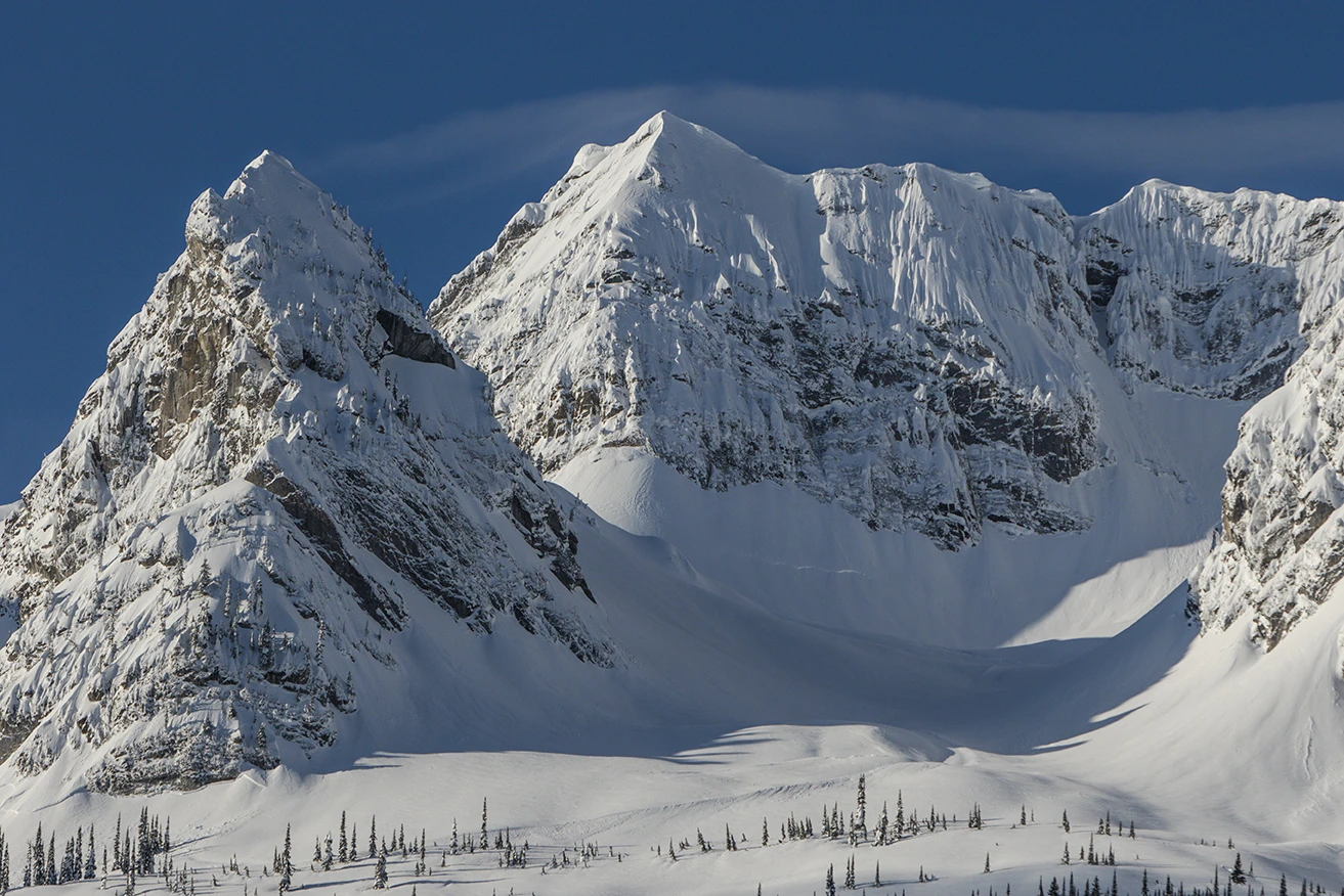 Snow-covered limestone peaks and a broad alpine bowl in the Lizard Range beneath a deep blue sky